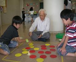 おじいさんに教わりながらカードゲームで遊んでいるこどもたちの様子の写真