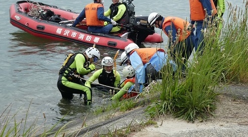 ボートに乗った隊員や別の隊員たちが岸から溺れた人を救出している写真