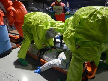 防護服を着た救助隊が負傷者を運ぶ
