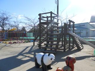 日差しが眩しい青空の下、アスレチック遊具のある園庭の写真